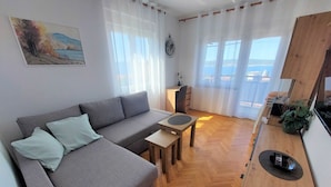 Una sala de estar moderna con un sofá gris, una mesa de centro de madera y vista al mar a través de amplios ventanales.