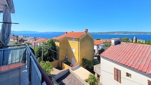 Un pueblo costero con edificios amarillos y techos rojos, un cielo azul despejado y vistas al mar y montañas distantes.