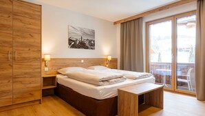 A bedroom with a wooden bed, a bench, a nightstand, and a large window with curtains. - Studio near the slopes with wellness area (Mittersill)