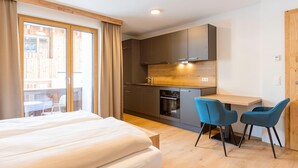 A modern hotel room with a large bed, a kitchenette, and a dining area with two chairs. - Studio near the slopes with wellness area (Mittersill)