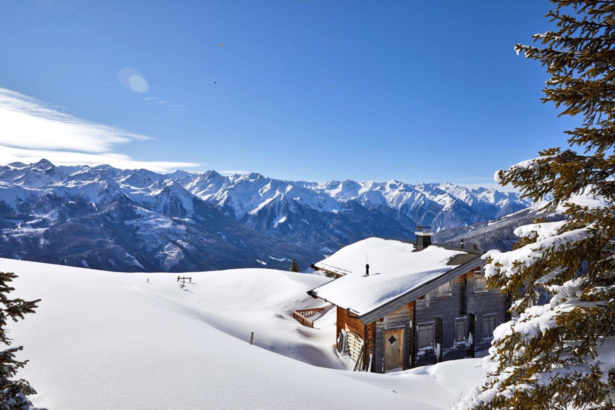 A snow-covered mountain landscape with a wooden cabin and a clear blue sky.