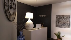 Et receptionsområde med en moderne lampe, en vase, en potteplante, et vægur og et indrammet kunstværk.