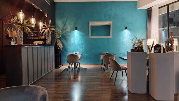 Et moderne spiseområde med en teal farvet væg, trægulv og moderne møbler.
