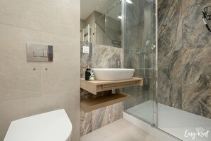 Features a sleek pedestal sink, glass-enclosed shower, and storage.