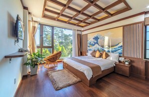 A bedroom with a large bed, wooden ceiling beams, a large window with a view of trees, a wall-mounted TV, and a traditional Japanese painting. - Khai Ngoc Hotel (Xuan Huong - Da Lat)