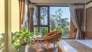 Una habitación con un ventanal grande, una silla de mimbre, una mesita pequeña y una planta en maceta.