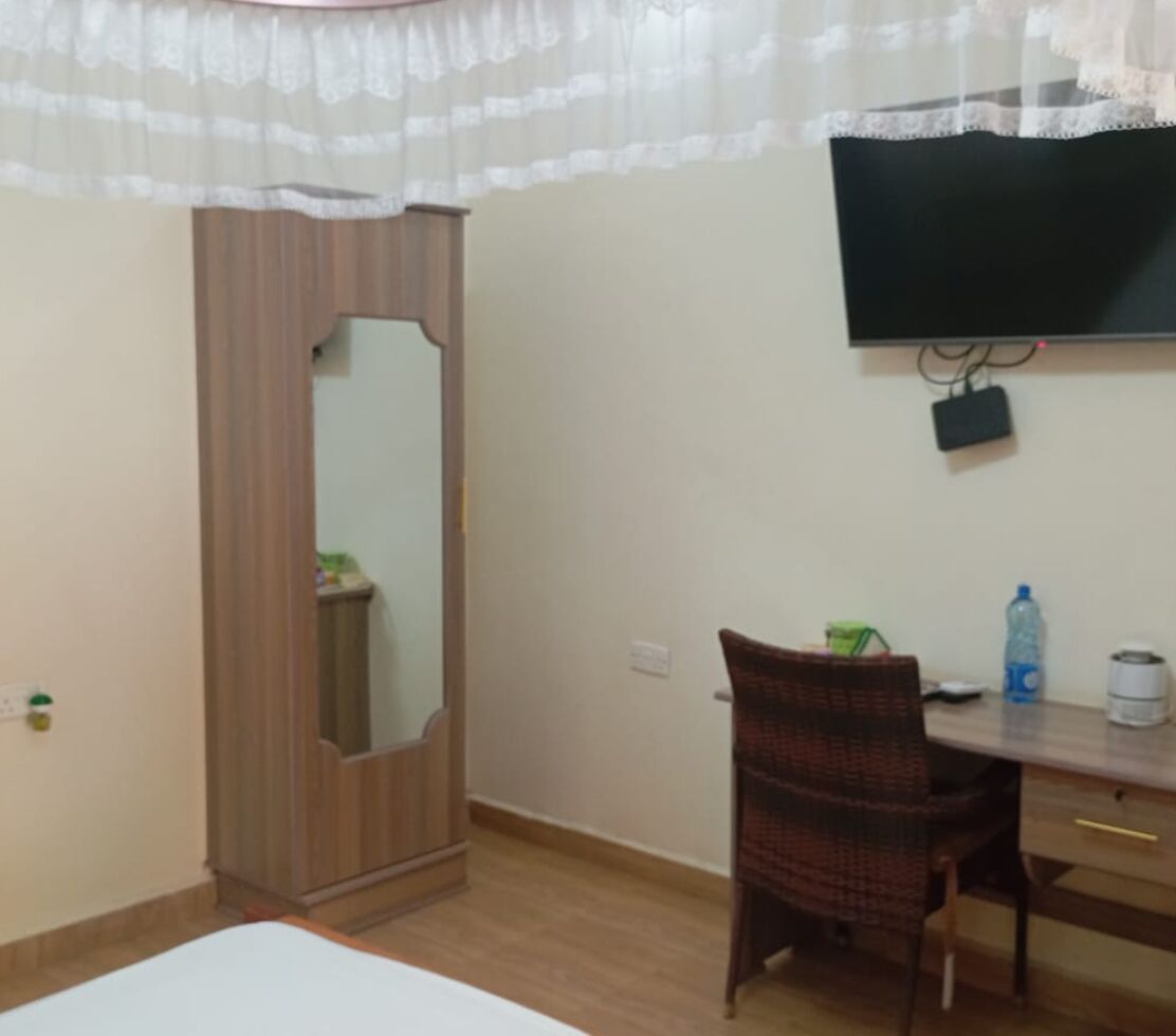 Una habitación con un armario de madera, un escritorio con una silla, un televisor montado en la pared y una cama.