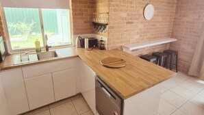 Una cocina con pared de ladrillo, encimera de madera, pileta, lavavajillas y ventana con vista a un patio trasero.