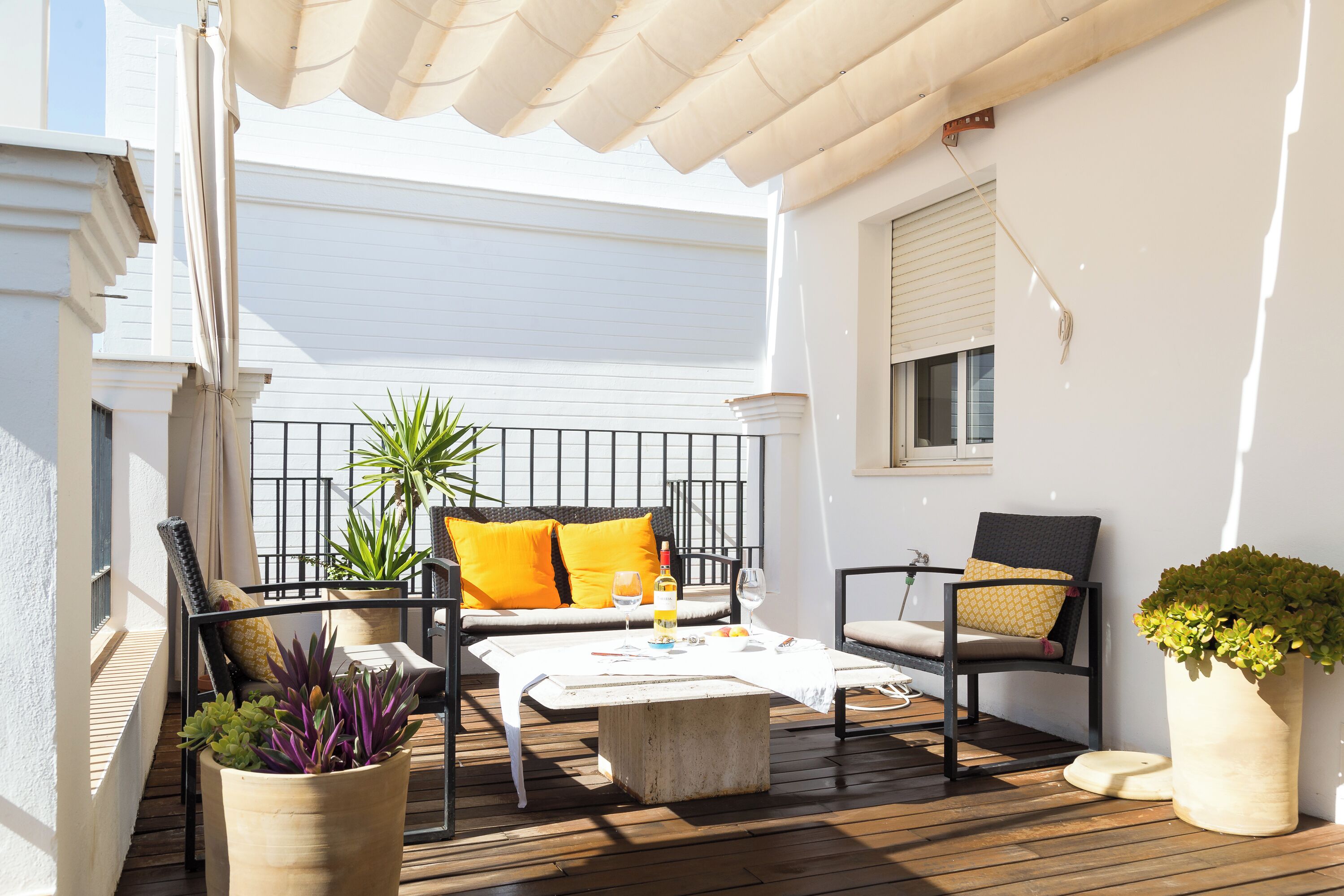 An outdoor patio with a wooden deck, a white table, two chairs, and a sofa with orange cushions.