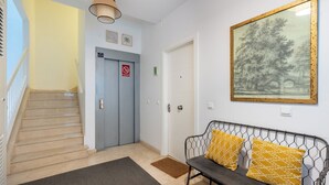 A hallway with a staircase, a bench with patterned cushions, a framed landscape painting, and a door with a 'No Smoking' sign. - Alhóndiga Ático. 1-bedroom, private terrace (Sevilla)