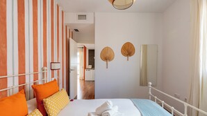 A hotel room with a bed, pillows, a bedside table, a mirror, and a view of the hallway. - Alhóndiga Ático. 1-bedroom, private terrace (Sevilla)