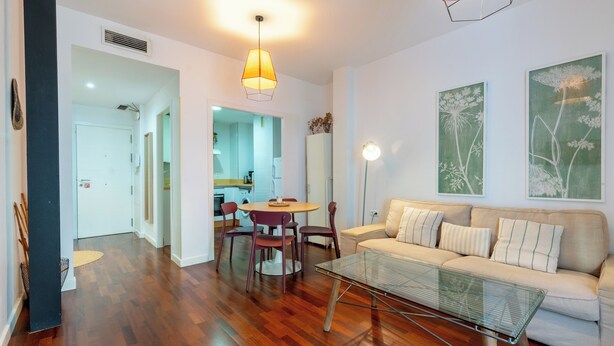 A modern living room with a sofa, a glass coffee table, and a dining area with a round table and chairs.