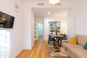 Un salon moderne avec un téléviseur à écran plat, une table basse en verre, un canapé beige et un coin repas comprenant des chaises et une table.
