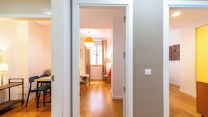 A hallway with wooden flooring, a dining area with a table and chairs, and a kitchen area with a stove.