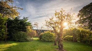 Un jardin bien entretenu, avec une variété d’arbres et d’arbustes, un chemin dégagé et un bâtiment visible au loin.