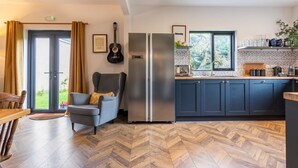 Une cuisine moderne avec un parquet en bois disposé en chevrons, un fauteuil gris, une guitare noire et une grande fenêtre.