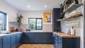 Une cuisine moderne avec des meubles de couleur bleu foncé, un parquet en bois disposé en chevrons et une grande fenêtre.