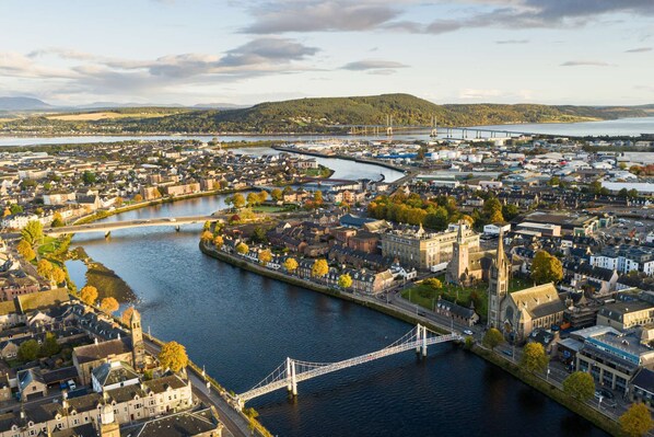 A river flowing through a town with a bridge, historic buildings, and a hilly landscape in the background.
