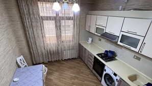 A compact kitchen with a dining area, built-in appliances, and a washing machine. - Victory Park Apartments (Baku)