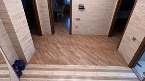 A spacious room with a wooden floor and a view of a dining area through an open door. - Victory Park Apartments (Baku)