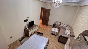 A spacious living room with a dining table, sofa, and a chandelier. - Victory Park Apartments (Baku)