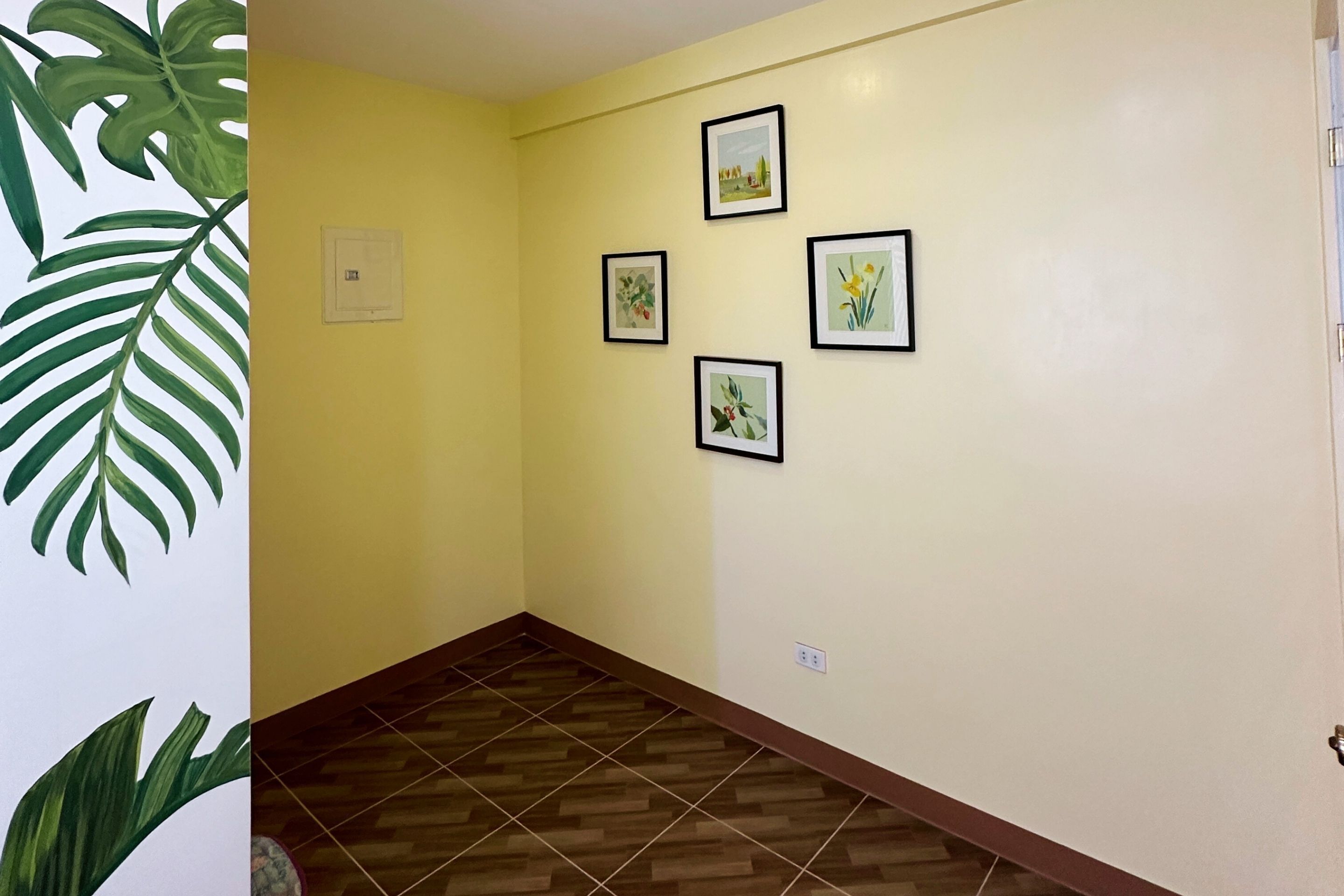 A hallway with a yellow wall, four framed pictures, and a wooden floor.