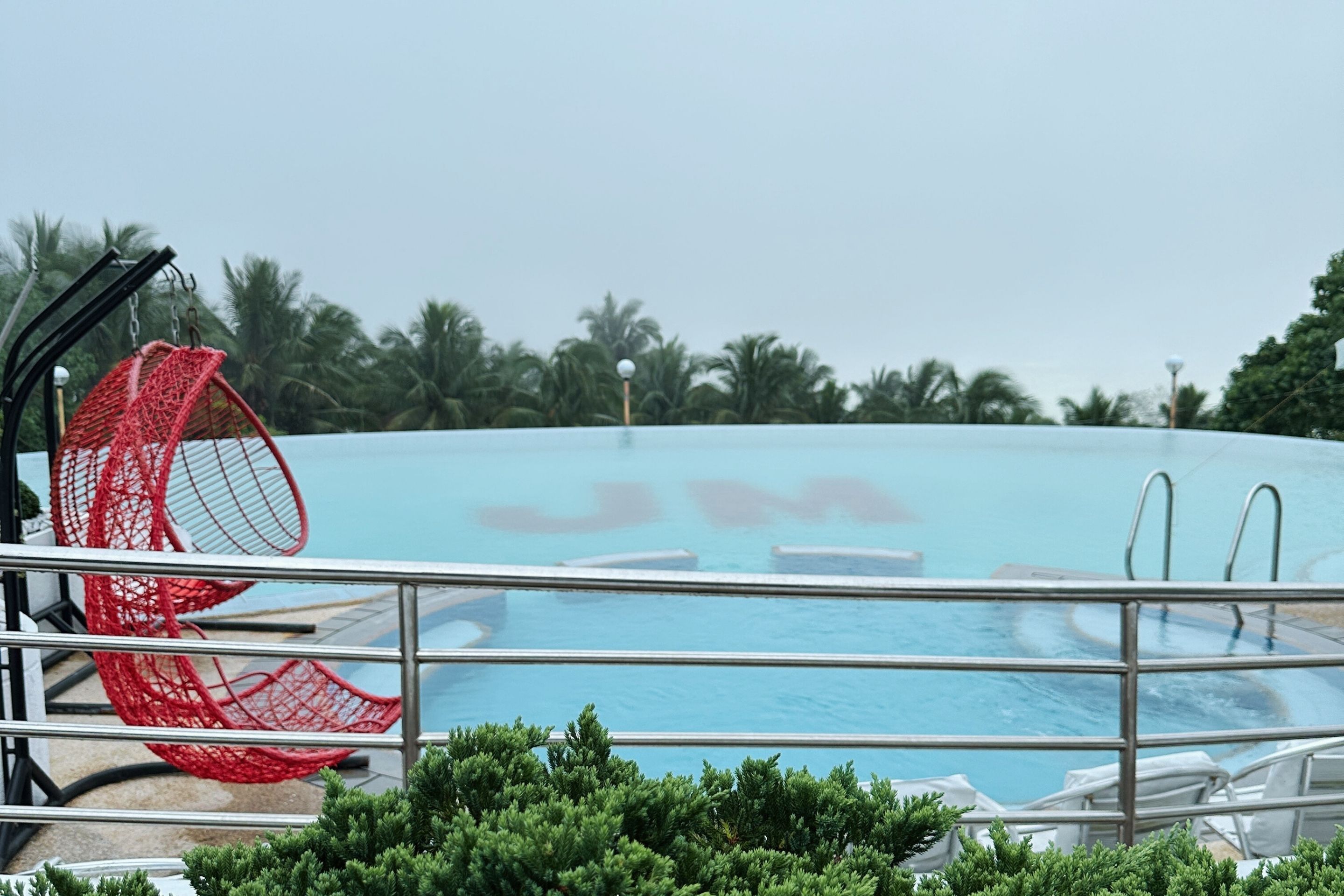 Un área de piscina con una silla roja, sillas de descanso y palmeras al fondo.