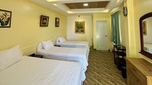 Ein Hotelzimmer mit drei Einzelbetten, einem Holzkoffer, einem Spiegel und einer Tür mit einem grünen Vorhang.