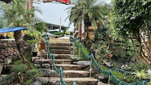 Eine Treppe aus Stein führt zu einem Gebäude, umgeben von üppigem Grün und Blumentöpfen.