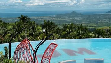 Una piscina con sillas rojas y vistas al océano y a las montañas.