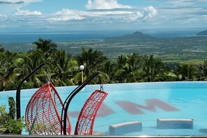 A pool with red chairs and a view of the ocean and mountains. - SMDP Resort Hotel CamSur (Ocampo)