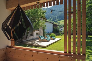 A wooden deck with a geometric metal shade, a wooden pergola, and a view of a green landscape with a house.