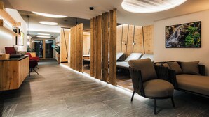 A modern interior with a wooden reception desk, a sofa, and a wall-mounted TV. - Ferienresidenz Raich (Ried im Oberinntal)