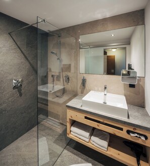 A modern bathroom with a glass-enclosed shower, a sink with a mirror, and a wooden vanity. - Ferienresidenz Raich (Ried im Oberinntal)