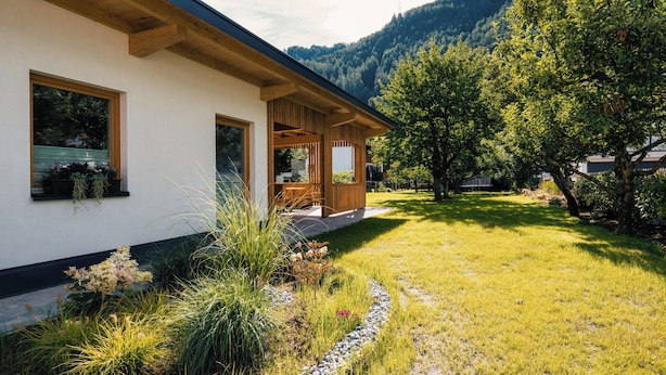 A modern house with a wooden exterior, a well-maintained lawn, and a mountain backdrop. - Ferienresidenz Raich (Ried im Oberinntal)