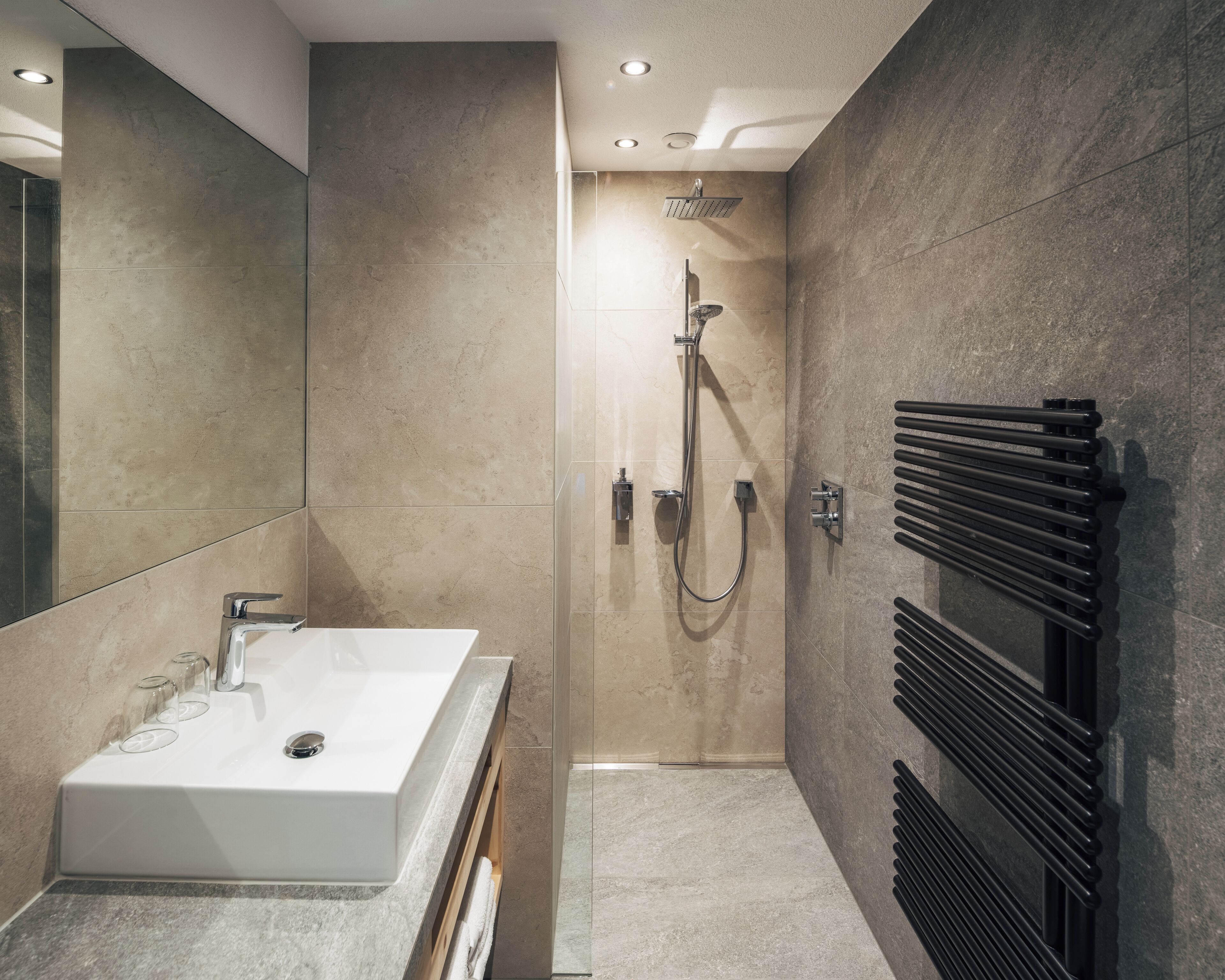 A modern bathroom with a large white sink, a handheld showerhead, and a towel rack.