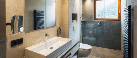 A modern bathroom with a large mirror, a white sink, a glass-enclosed shower, and a view of the outdoors through a window.