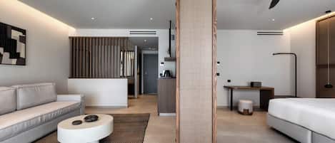 Una habitación de hotel moderna con sofá, una mesa redonda, cama, escritorio y un ventanal grande.