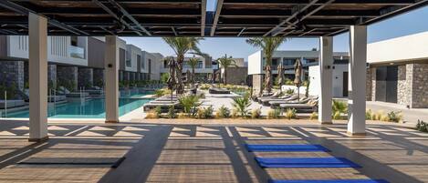 A covered outdoor area with a pool, sun loungers, and exercise mats.