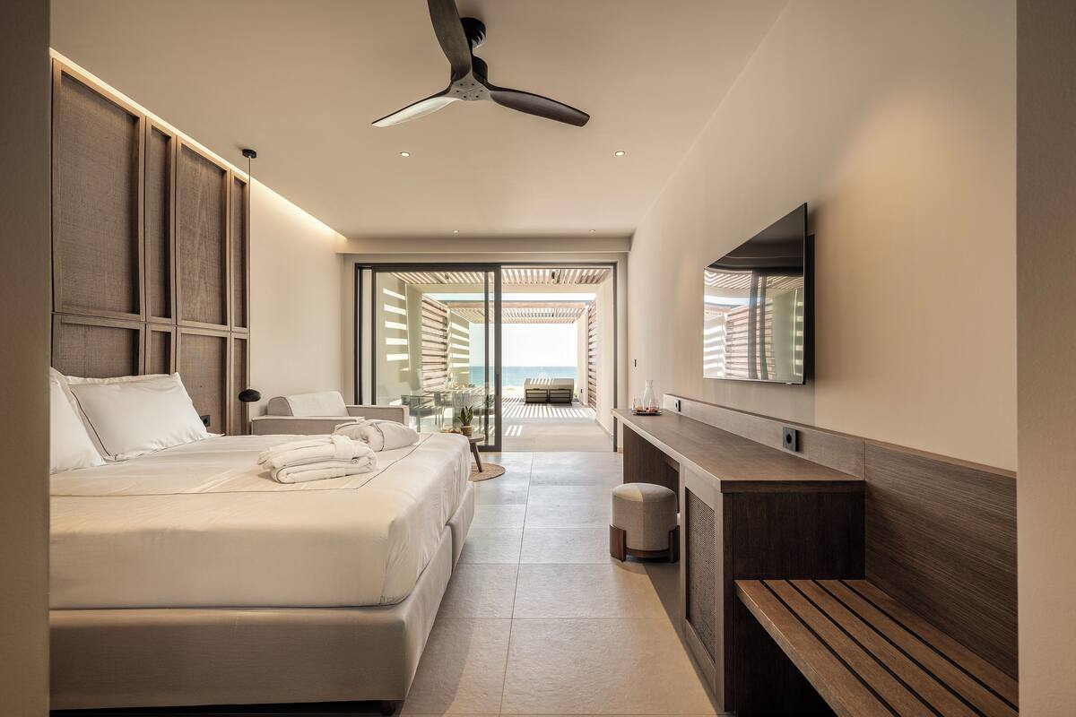 A modern hotel room with a large bed, a desk, a bench, and a ceiling fan.