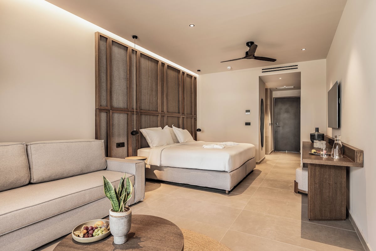 A modern bedroom with a bed, a sofa, a bedside table, and a potted plant.