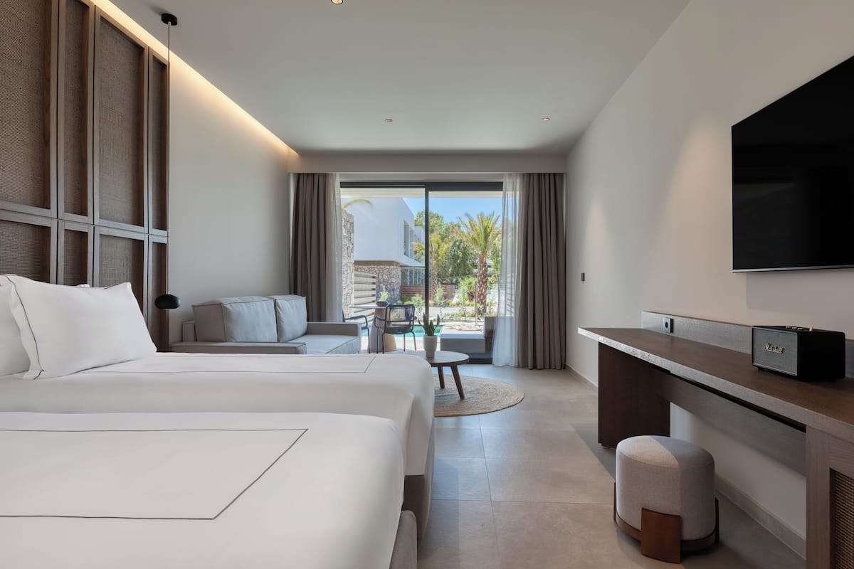 A hotel room with two beds, a desk, a TV, and a balcony with a view of the outside.