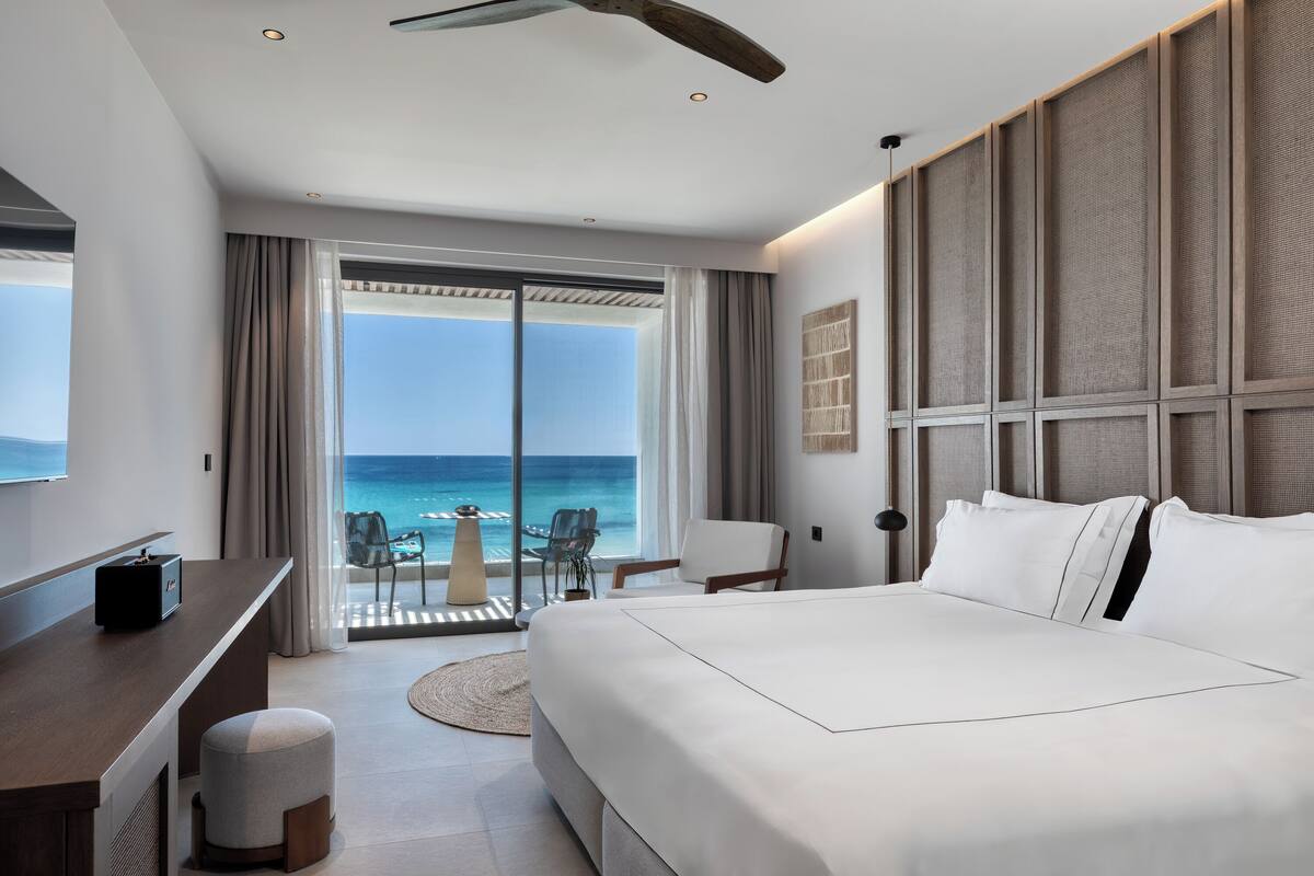 A modern hotel room with a large bed, a desk, and a view of the ocean.