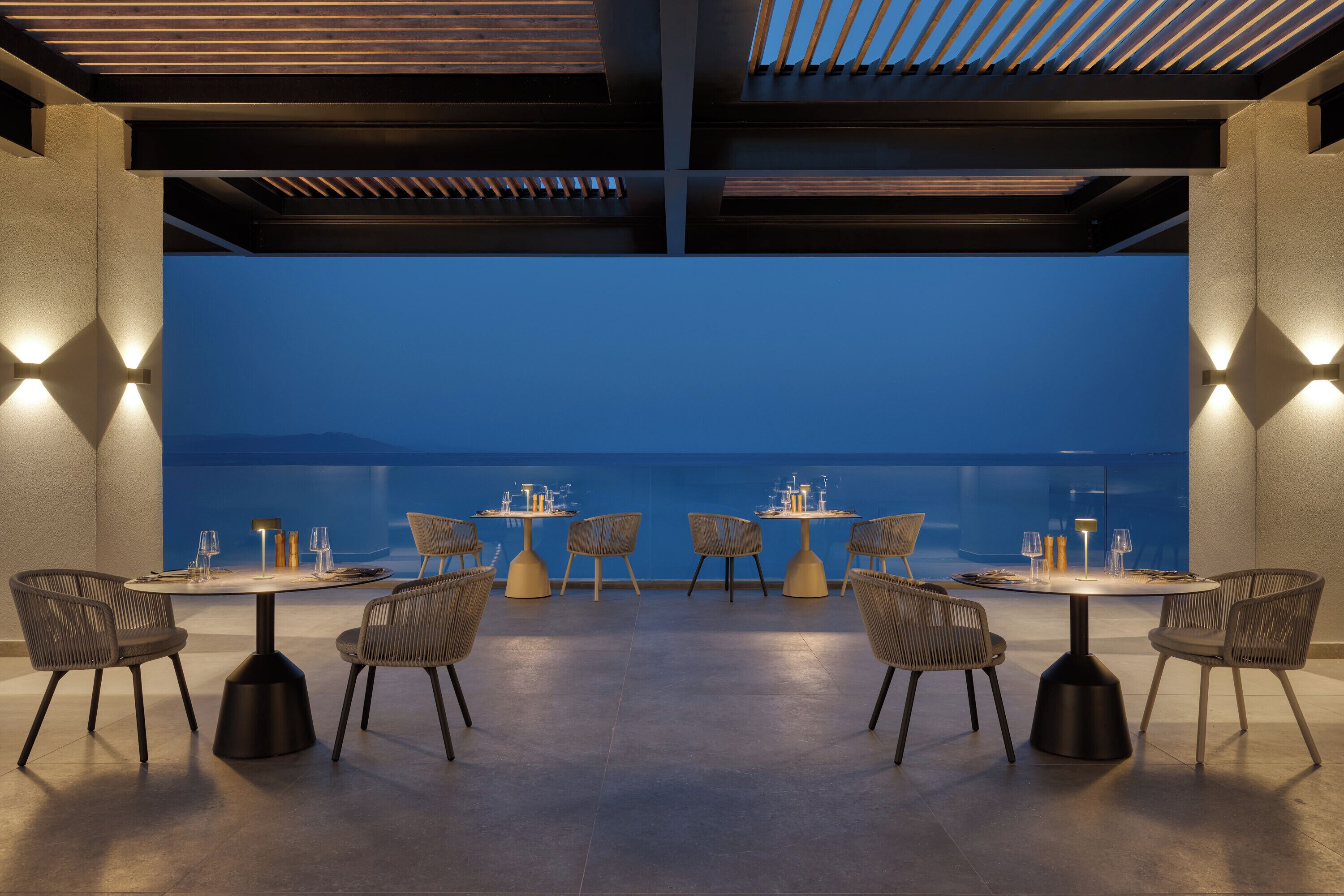 A rooftop dining area with round tables and chairs, a view of the cityscape, and a modern architectural design.