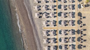 An aerial view of a beach with rows of umbrellas and lounge chairs, indicating a resort area. - Mosay All Suite Hotel - Adults friendly (Kos)