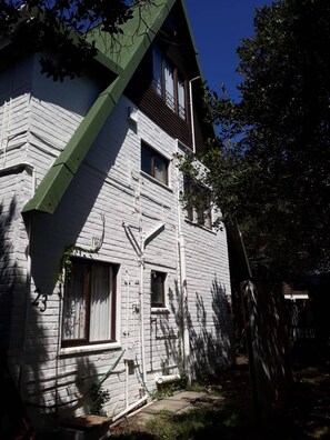 Un edificio de dos plantas con techo verde y paredes exteriores blancas. Se observan varias ventanas y una chimenea.