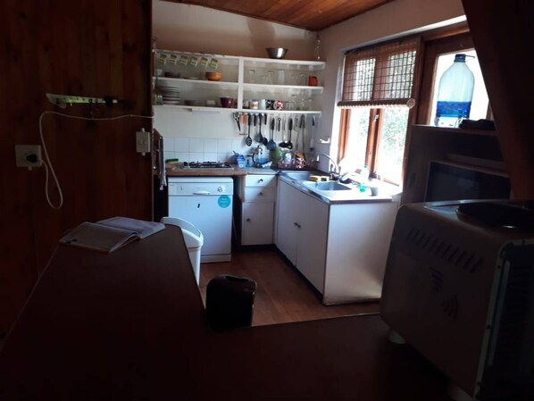 Una cocina compacta con armarios blancos, un lavamanos y una estufa. Hay una ventana con persianas, un dispensador de agua y un microondas.