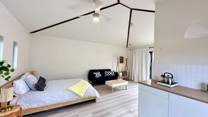 Ein modernes Zimmer mit einem Bett, einer schwarzen Couch, einem kleinen Tisch und einer Küchenzeile mit einem Wasserkocher.