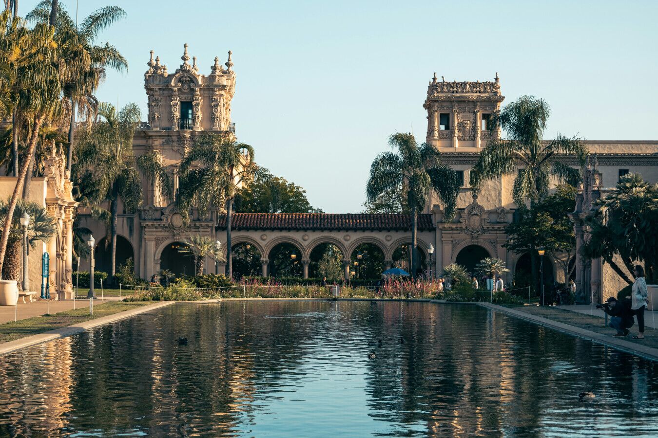 Un edificio histórico con arquitectura ornamentada, un estanque reflectante y palmeras.