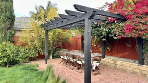 Eine Terrasse mit einer Holzpergola, einem Esstisch mit Stühlen und einem roten Zaun.